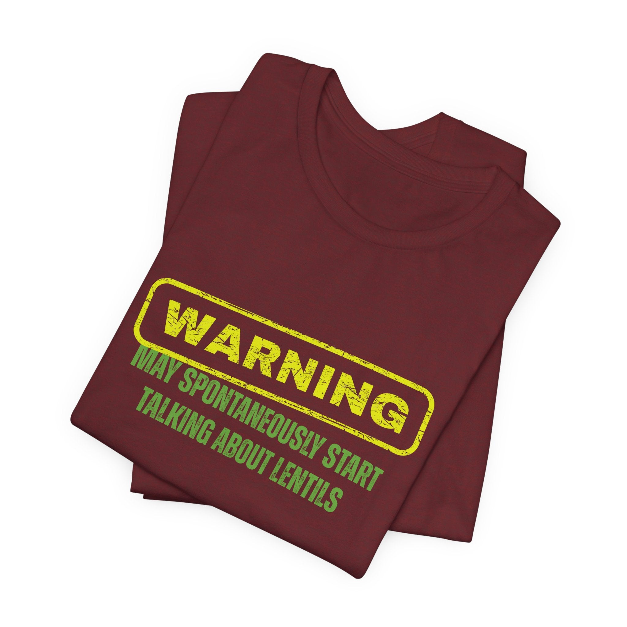 Folded maroon t-shirt with yellow and green text "Warning - may spontaneously start talking about lentils" by Soon To Be Mythical