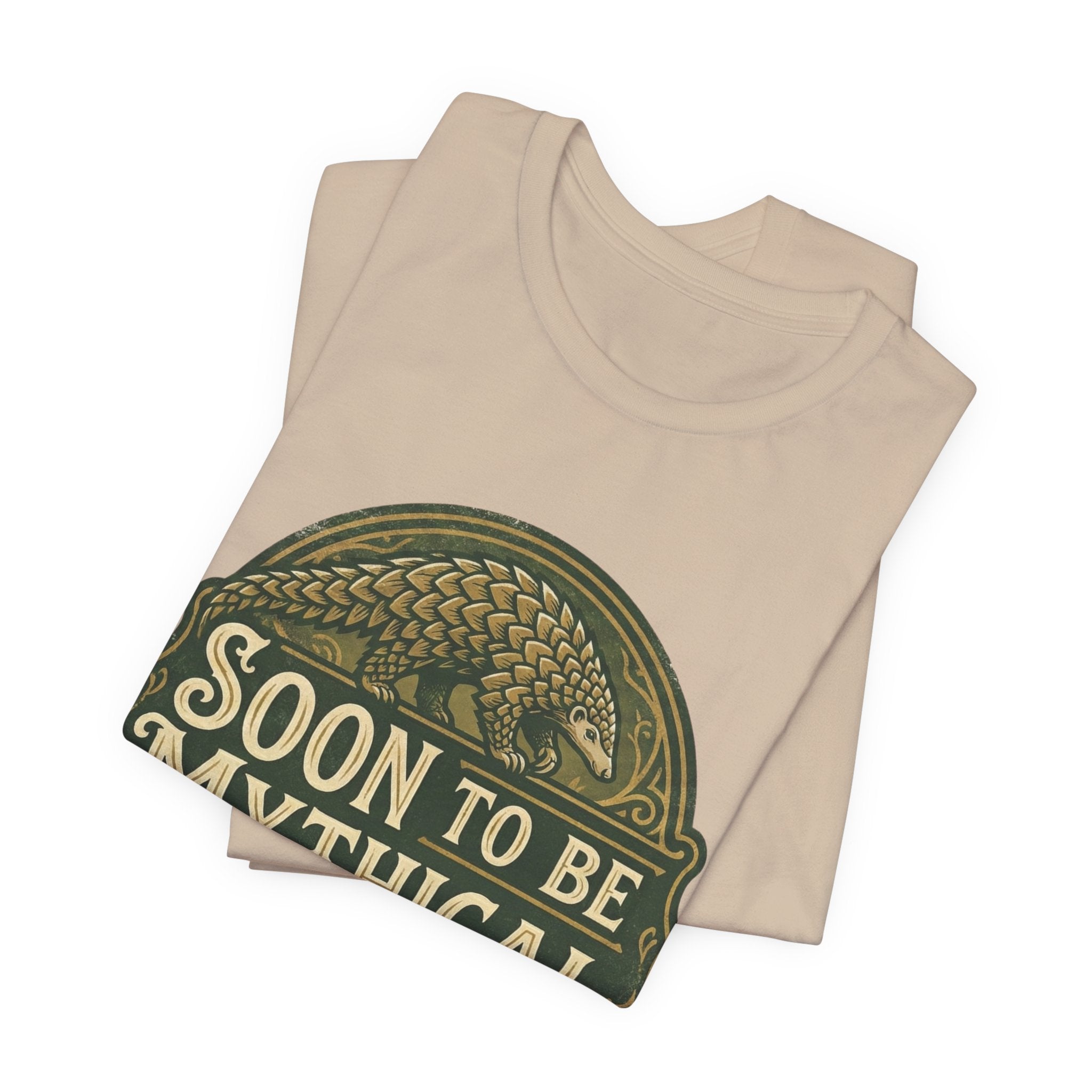 Folded beige t-shirt with 'Soon to be Mythical' vintage logo with a pangolin on a white background