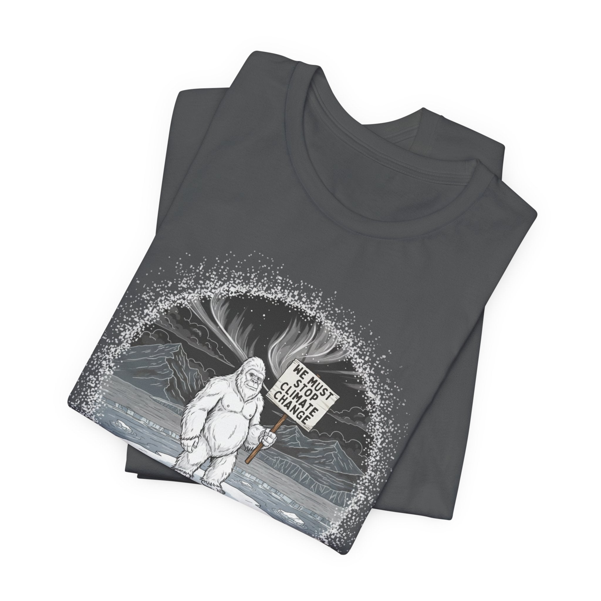 Folded gray t-shirt with a graphic of a Yeti on an ice floe holding a sign with the text "We must stop climate change" by Soon To Be Mythical