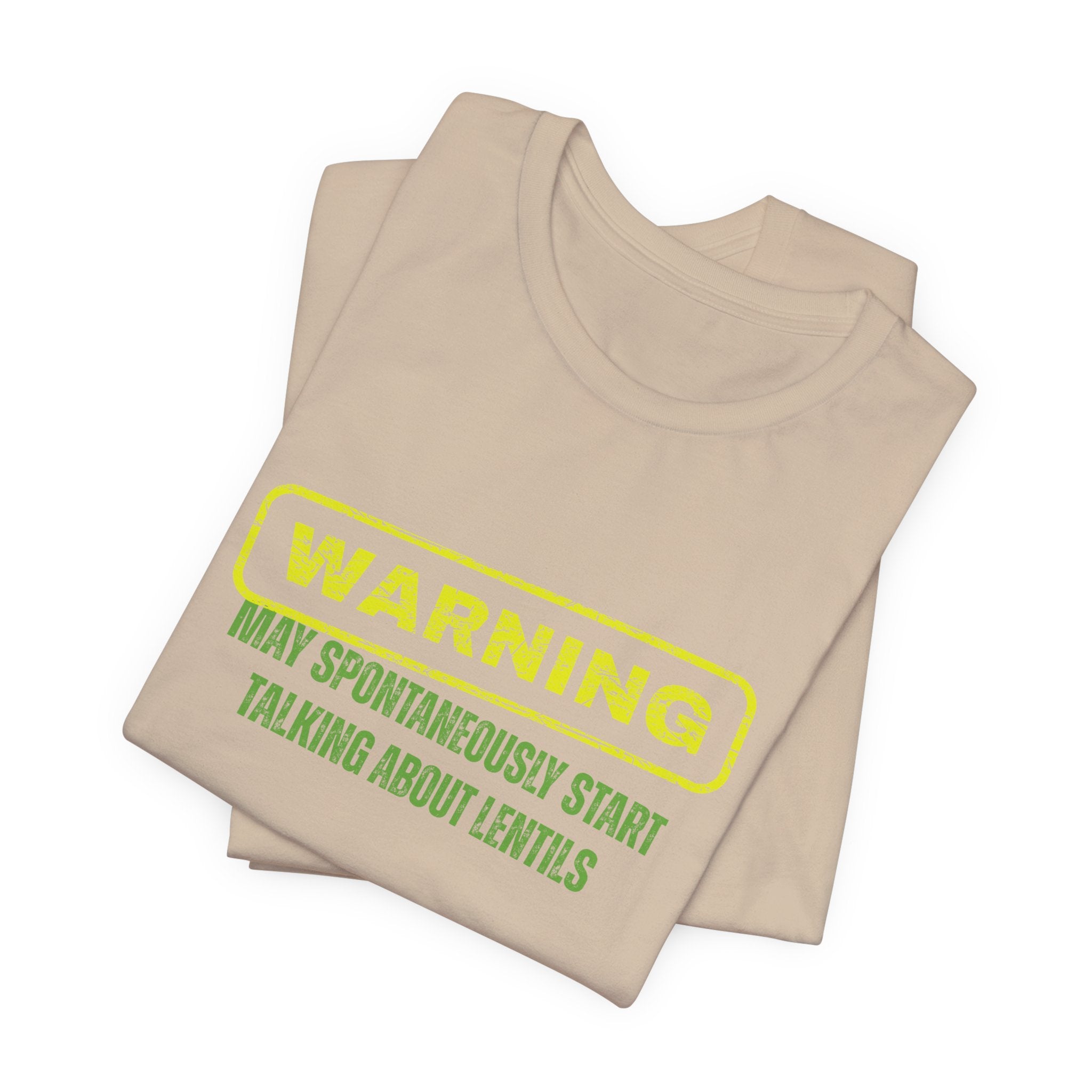 Folded beige t-shirt with yellow and green text "Warning - may spontaneously start talking about lentils" by Soon To Be Mythical