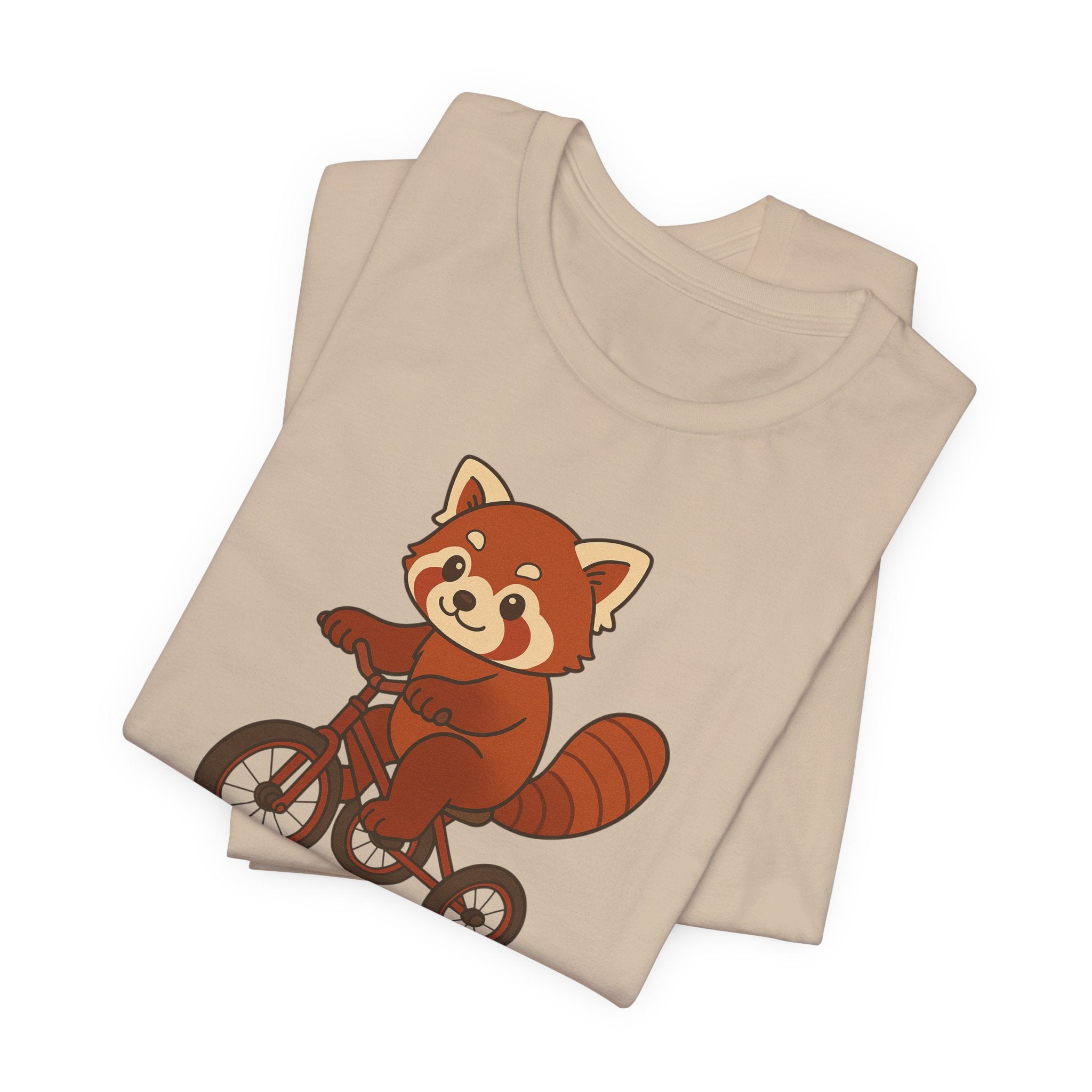Folded tan  t-shirt with a red panda riding a tricycle graphic on a white background