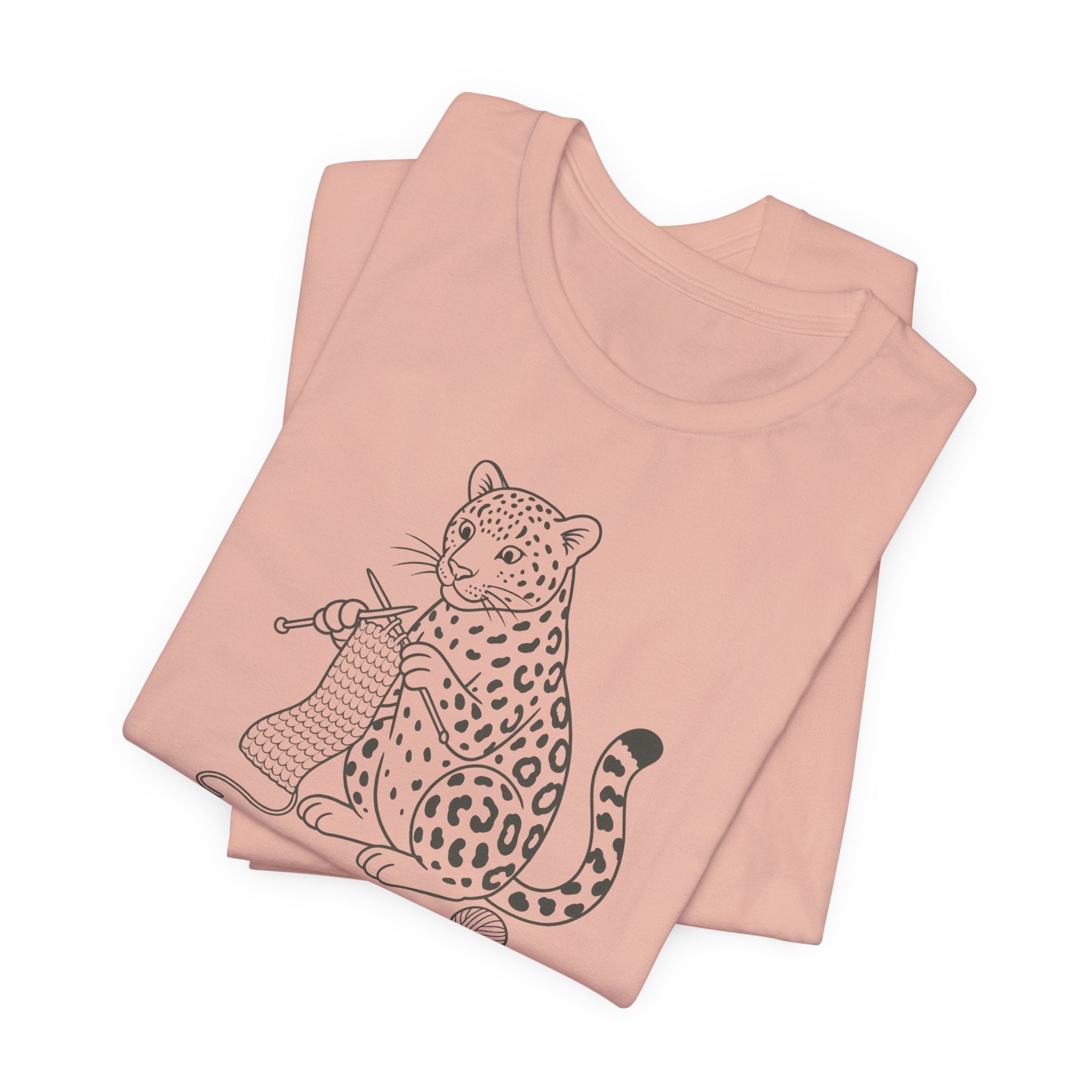 Folded peach t-shirt with a leopard knitting a scarf on a white background