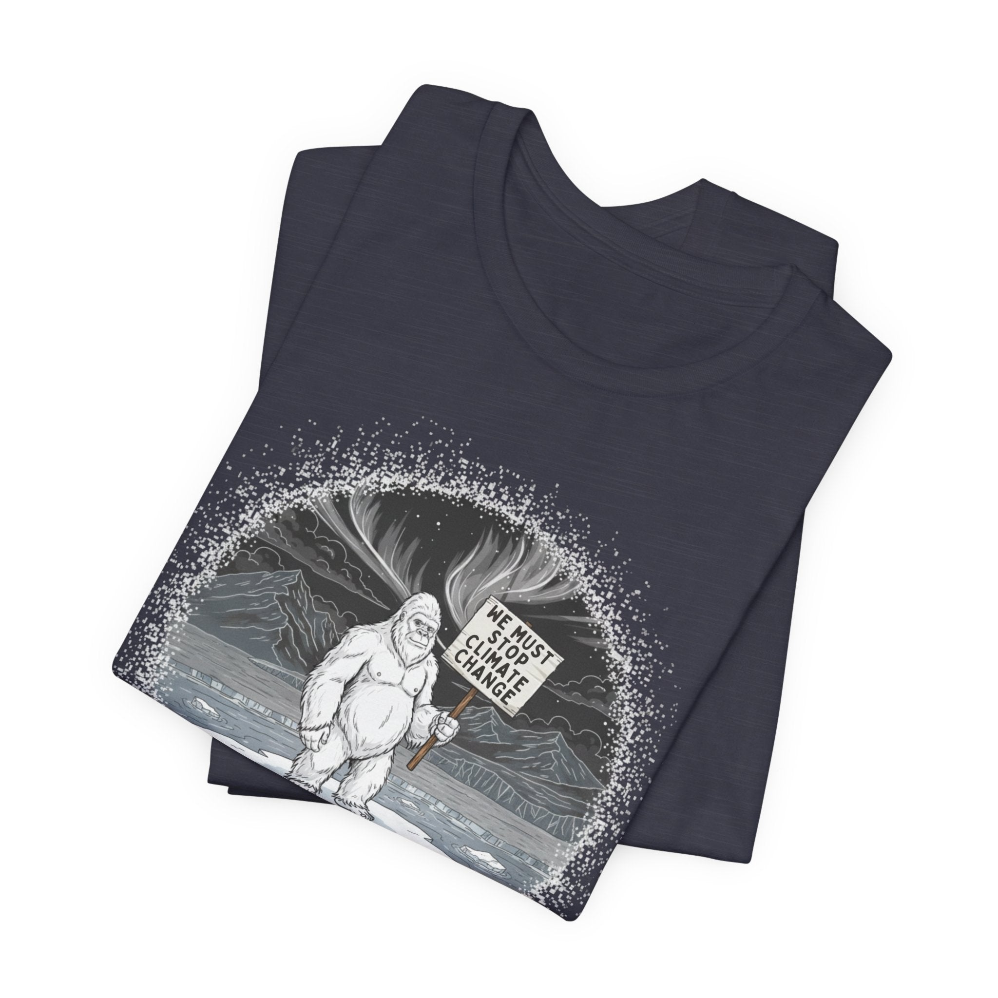 Folded gray t-shirt with a graphic of a Yeti on an ice floe holding a sign with the text "We must stop climate change" by Soon To Be Mythical