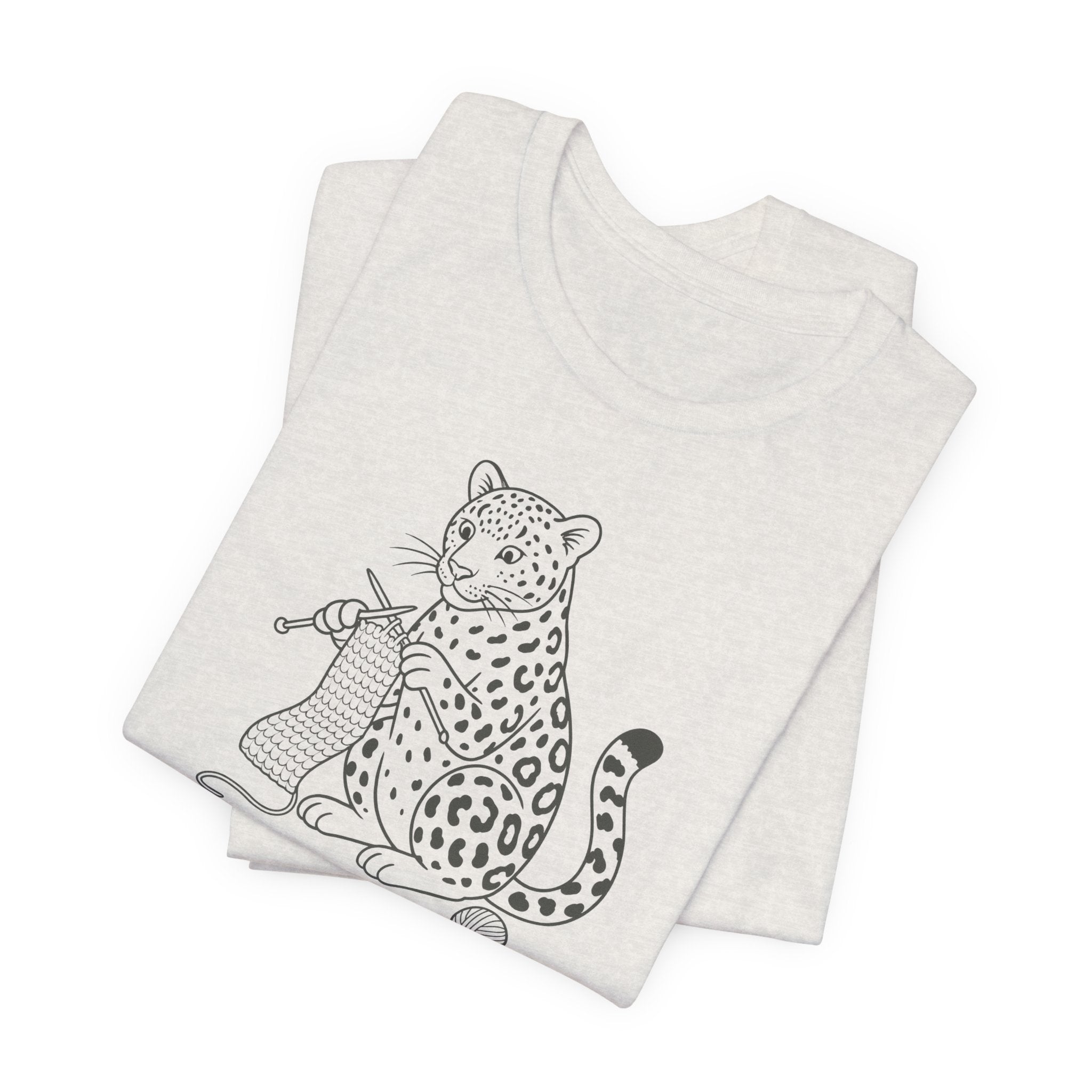 Folded heathered cement t-shirt with a black and white illustration of a leopard knitting a scarf on a white background