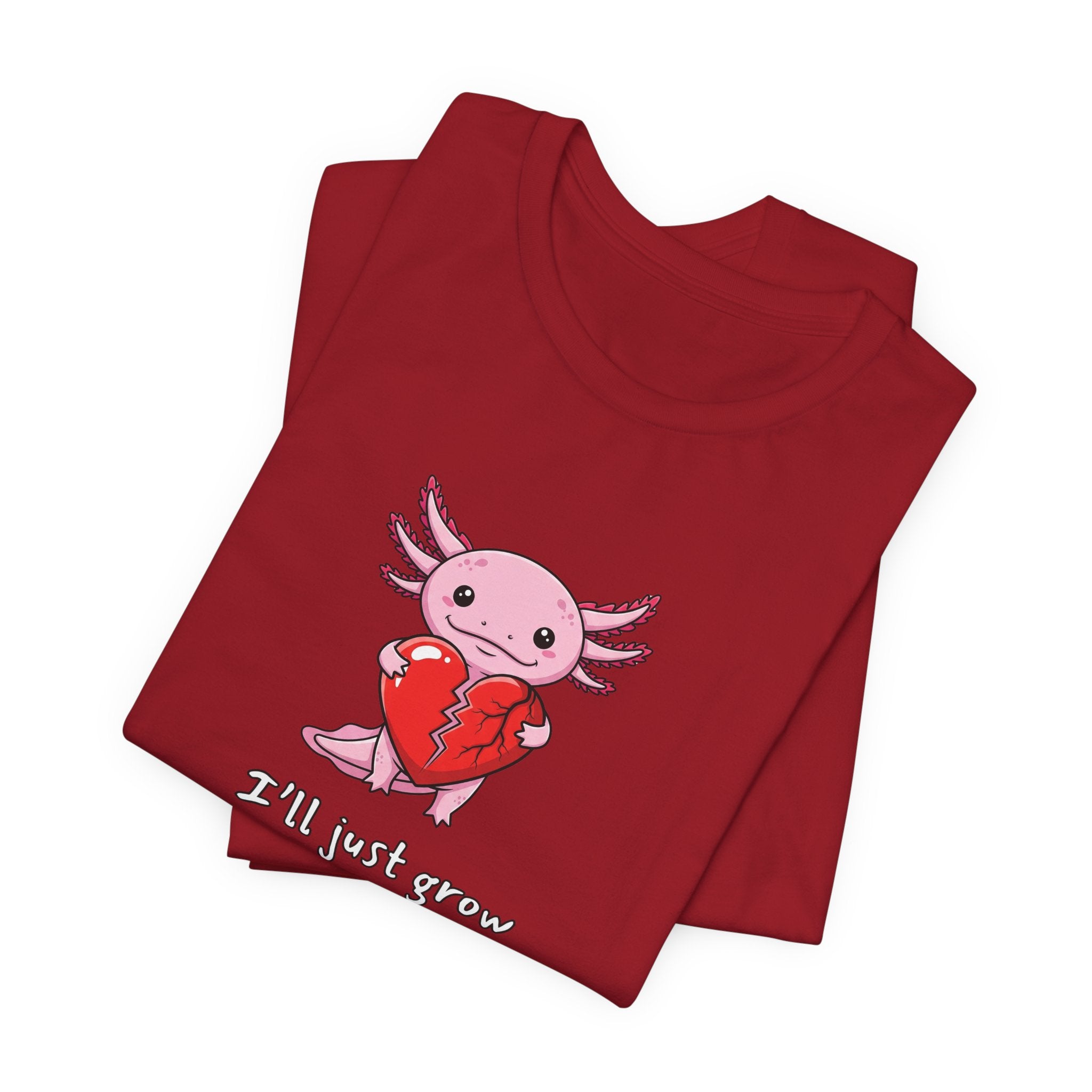 Folded red t-shirt with axolotl graphic with a broken heart and text "I'll just grow a new one" by Soon To Be Mythical