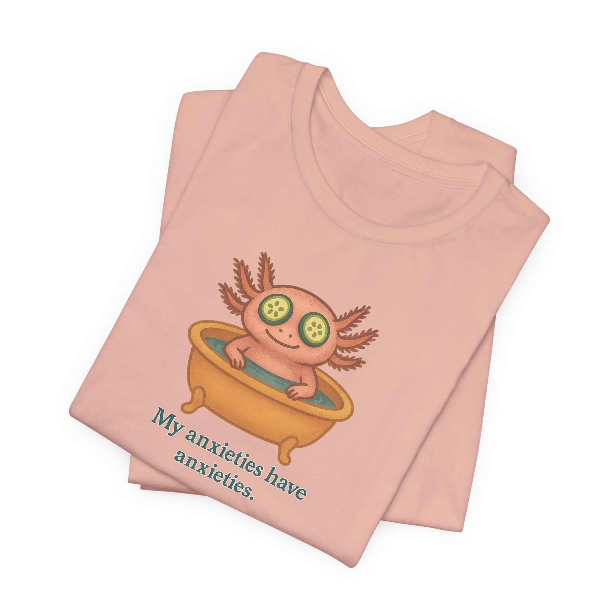 Folded peach t-shirt with a cartoon axolotl and text "My anxieties have anxieties" on a white background