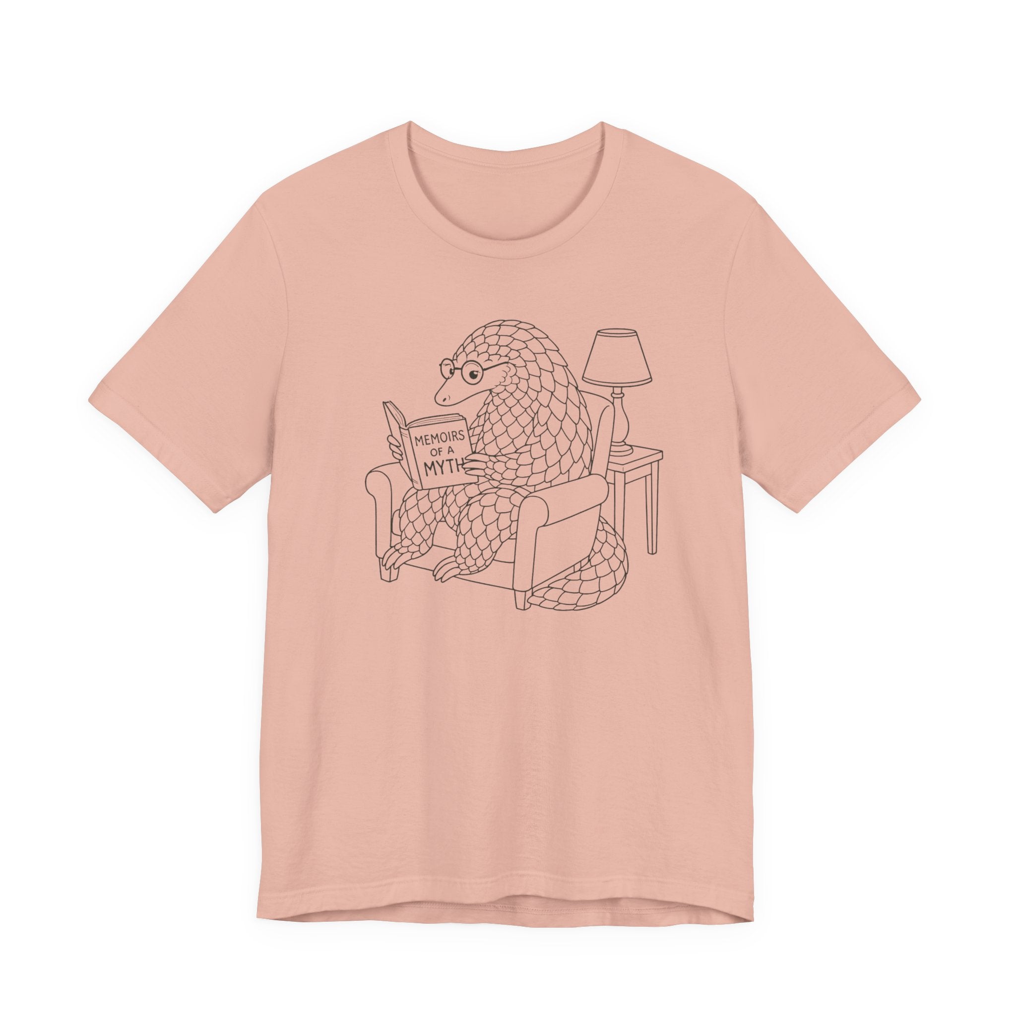 Peach t-shirt with a graphic of a pangolin reading a book titled 'Memoirs of a Myth' on a white background.