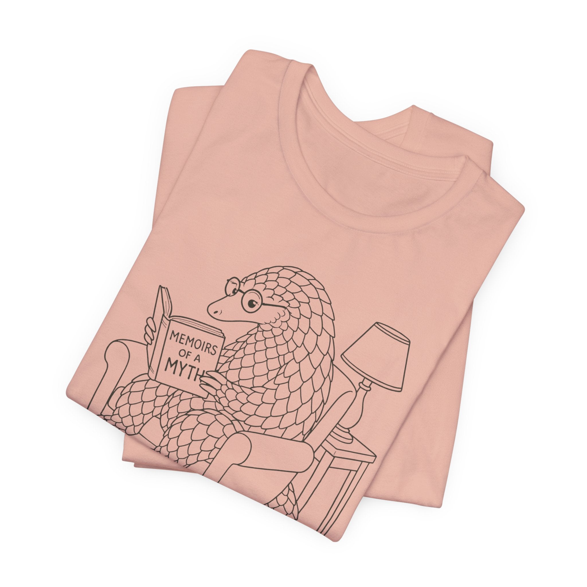 Folded peach t-shirt with a graphic of a pangolin reading 'Memoirs of a Myth' on a white background